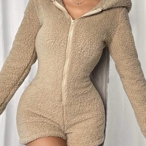 May include: A beige, hooded romper with a full-length zipper and short shorts. The romper is made of a soft, textured material. The long sleeves and hood provide warmth, while the shorts offer a casual look. The outfit is designed for comfort and style.