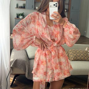May include: A two-piece set consisting of a long-sleeved, open-front kimono-style jacket and matching shorts, both featuring a watercolor-inspired abstract print in shades of coral, peach, and white on a sheer, lightweight fabric.