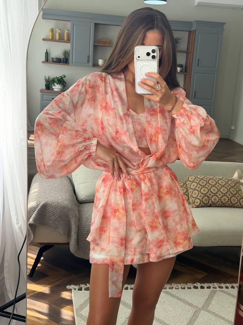 May include: A two-piece set consisting of a long-sleeved, open-front kimono-style jacket and matching shorts, both featuring a watercolor-inspired abstract print in shades of coral, peach, and white on a sheer, lightweight fabric.