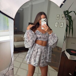 May include: A two-piece set consisting of a cropped camisole top and matching high-waisted shorts, both featuring a sheer, lightweight fabric with a grey and blue abstract floral print. The top has thin straps, and the shorts have an elastic waistband.