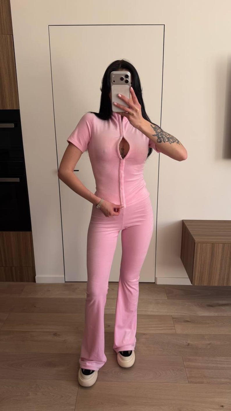 Puede incluir: Mono rosa claro con top de manga corta y pantal&oacute;n acampanado. El mono tiene una cremallera en la parte delantera y est&aacute; hecho de un material suave y aterciopelado. El modelo lleva zapatillas blancas con plataforma.