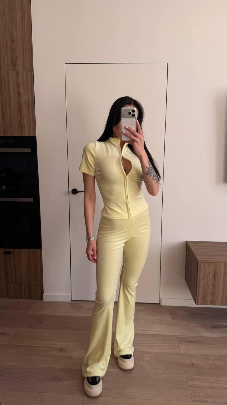 Puede incluir: Mono amarillo claro con cuello alto, mangas cortas y cremallera frontal. El mono tiene un corpi&ntilde;o ajustado y pantalones acampanados. La persona lleva zapatillas blancas. El conjunto est&aacute; hecho de un tejido suave y aterciopelado.
