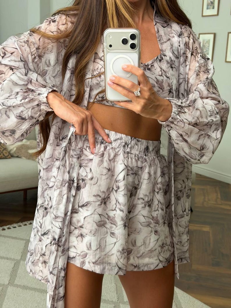 May include: A three-piece set consisting of a long-sleeved, open-front duster cardigan, a cropped tank top, and high-waisted shorts. The garments are made of a lightweight, sheer fabric featuring a monochromatic gray and white floral print.