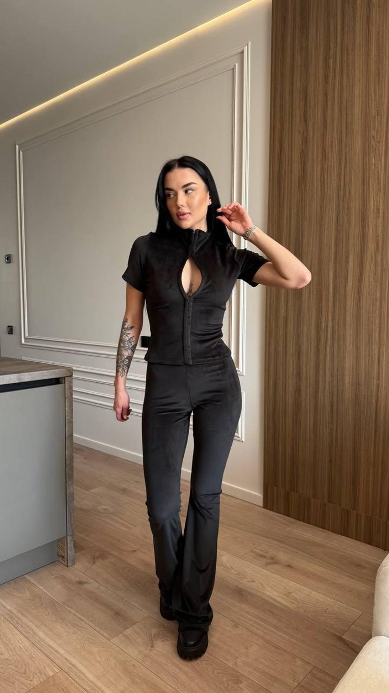 Puede incluir: Conjunto negro de dos piezas. La parte superior tiene mangas cortas, cuello alto y un corte de ojo de cerradura. Los pantalones son acampanados. El conjunto est&aacute; hecho de un material suave y aterciopelado. El modelo lleva zapatos negros.