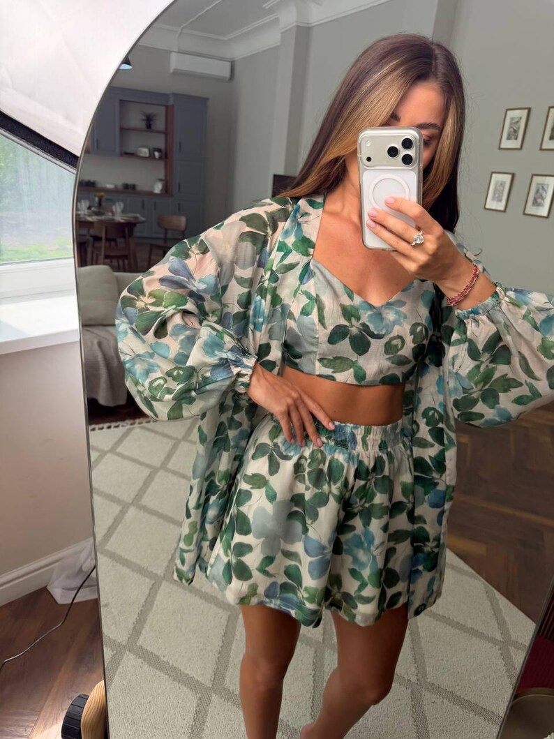 May include: A three-piece matching set featuring a cropped camisole top, high-waisted shorts with an elastic waistband, and a long-sleeved button-down shirt. The garments are made of a sheer, lightweight fabric with a green and blue leaf print.