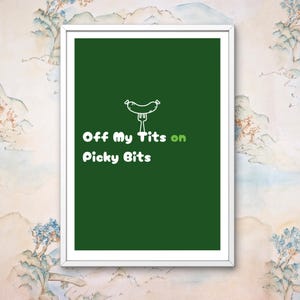 May include: A framed print with a dark green background and white text that reads "Off My Tits on Picky Bits." A cartoon sausage on a fork is above the text. The frame is white.