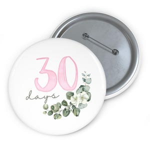 May include: White button with the text "30 days" in pink and gray script. The button features a floral design with white flowers and green leaves. The button has a silver metal backing and a pin.