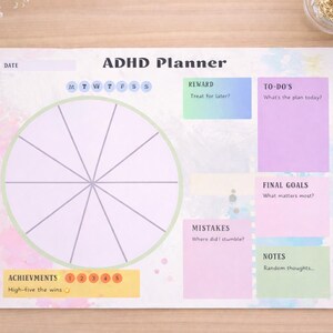 Könnte beinhalten: ADHS-Planer mit Raddesign, To-Do-Listen und Zielabschnitten. Der Planer enthält Abschnitte für Belohnungen, Fehler und Notizen. Auf einer Holzoberfläche mit Schreibwaren.