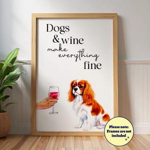 May include: A framed print with the text "Dogs & wine make everything fine." The artwork features a Cavalier King Charles Spaniel and a hand holding a glass of red wine. The frame is a light wood color.