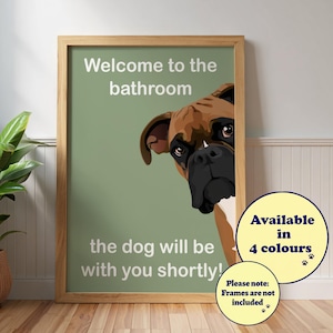 May include: A framed print with a brown and white Boxer dog peeking out from behind the frame. The text reads "Welcome to the bathroom, the dog will be with you shortly!" A circular graphic states "Available in 4 colours."