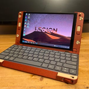 May include: A red and gray laptop with the word "LEGION" on the screen. The laptop is open, displaying a desktop background with a desert landscape and starry sky. The keyboard is gray, and the frame is red.