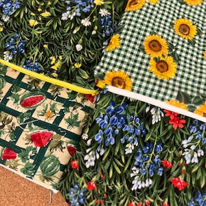 May include: Four fabric pouches with floral and fruit patterns. One pouch features sunflowers on a green and white checkered background. Another has a watermelon design. The other two pouches have floral patterns with blue, yellow, and red flowers.