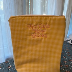Puede incluir: Bolso tote de cuadros amarillos con cierre de cremallera. La bolsa presenta el texto bordado "Hot Girls Read Books" en una fuente cursiva. La bolsa est&aacute; hecha de una tela suave y est&aacute; dise&ntilde;ada para llevar libros.