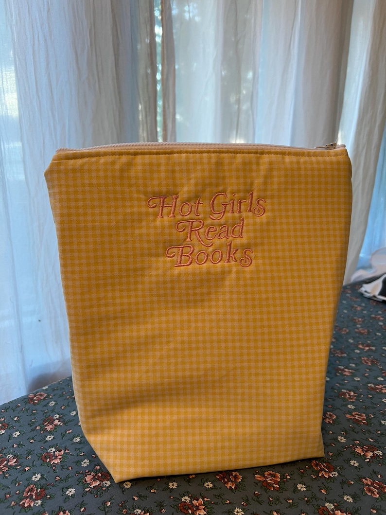 Puede incluir: Bolso tote de cuadros amarillos con cierre de cremallera. La bolsa presenta el texto bordado "Hot Girls Read Books" en una fuente cursiva. La bolsa est&aacute; hecha de una tela suave y est&aacute; dise&ntilde;ada para llevar libros.