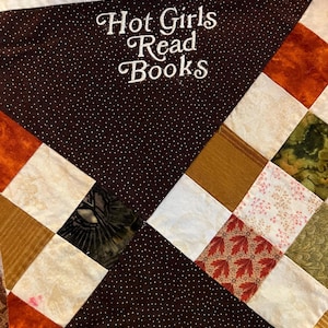 Puede incluir: Un edred&oacute;n hecho a mano con una secci&oacute;n marr&oacute;n con lunares bordada con las palabras "Hot Girls Read Books" en escritura blanca. El edred&oacute;n presenta un dise&ntilde;o de patchwork con cuadrados de varios colores y patrones, incluyendo estampados naranjas, blancos y florales.