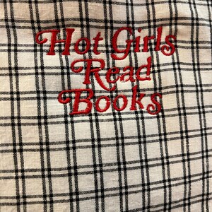 Puede incluir: Tela blanca con un patr&oacute;n de cuadros negros. Las palabras "Hot Girls Read Books" est&aacute;n bordadas en rojo. La tela tiene un aspecto ligeramente texturizado.