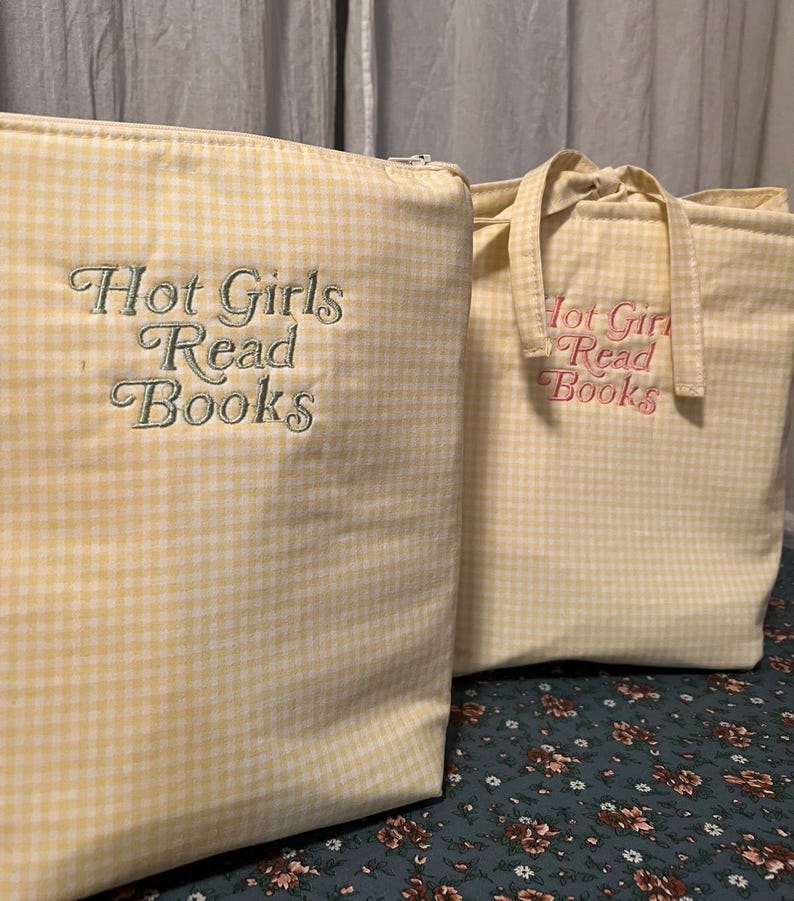 Puede incluir: Dos bolsas de tela de cuadros amarillos. Una es un estuche con cremallera con el texto bordado "Hot Girls Read Books" en verde. La otra es una bolsa de mano con el mismo texto en rosa. Ambas bolsas tienen un estampado de cuadros amarillos claros y blancos.