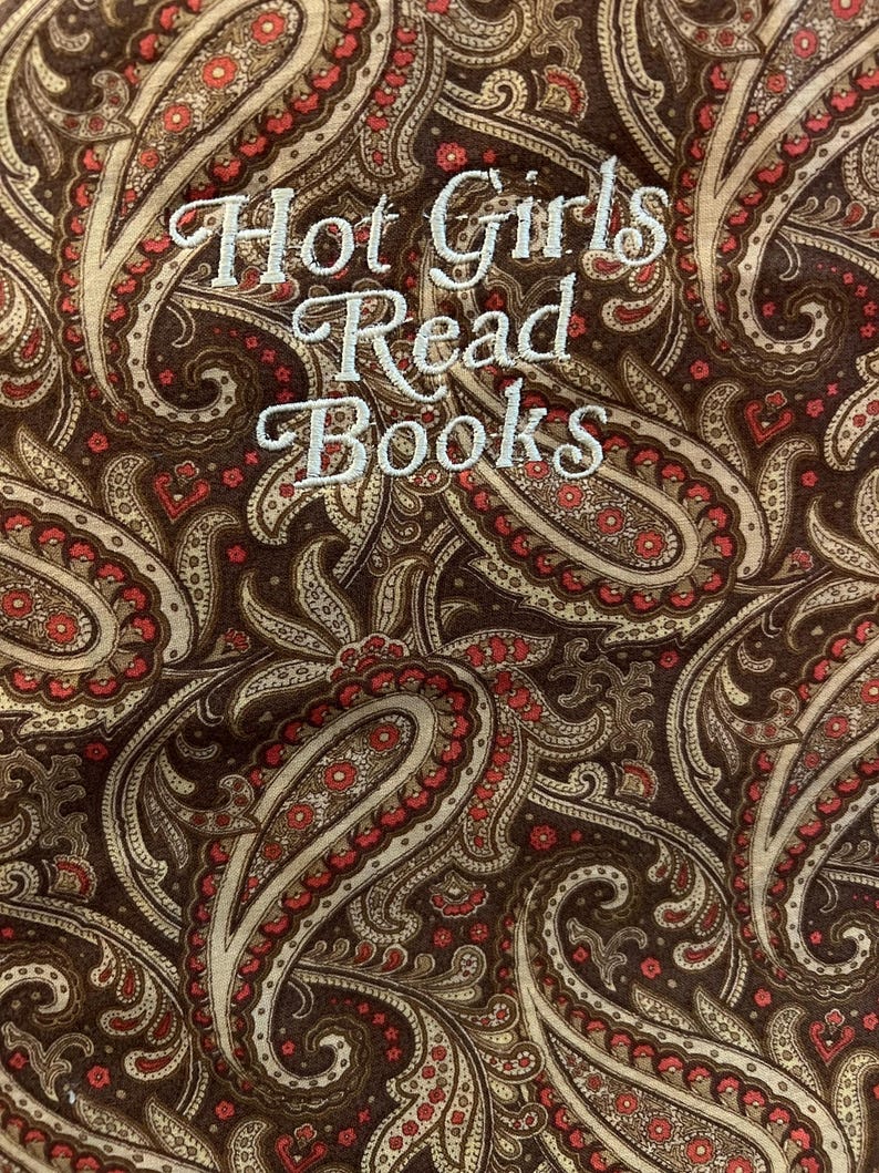 Puede incluir: Una tela estampada con un dise&ntilde;o de cachemira en tonos marr&oacute;n, beige y rojo. El texto "Hot Girls Read Books" est&aacute; bordado en blanco. El dise&ntilde;o es detallado e intrincado, con una est&eacute;tica vintage.