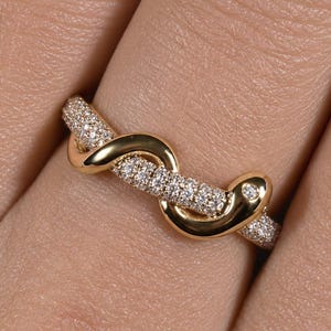 Op de afbeelding: Een gouden ring in de vorm van een kronkelende slang, met een gepolijste gouden kop en staart en een lichaam ingelegd met kleine, heldere pavé-gezette steentjes. Het ontwerp wikkelt zich om de vinger en toont een mix van glad metaal en glinstering.