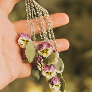May include: A silver ear cuff with multiple chains and purple and white flower charms. The flowers are made of polymer clay and resemble pansies.