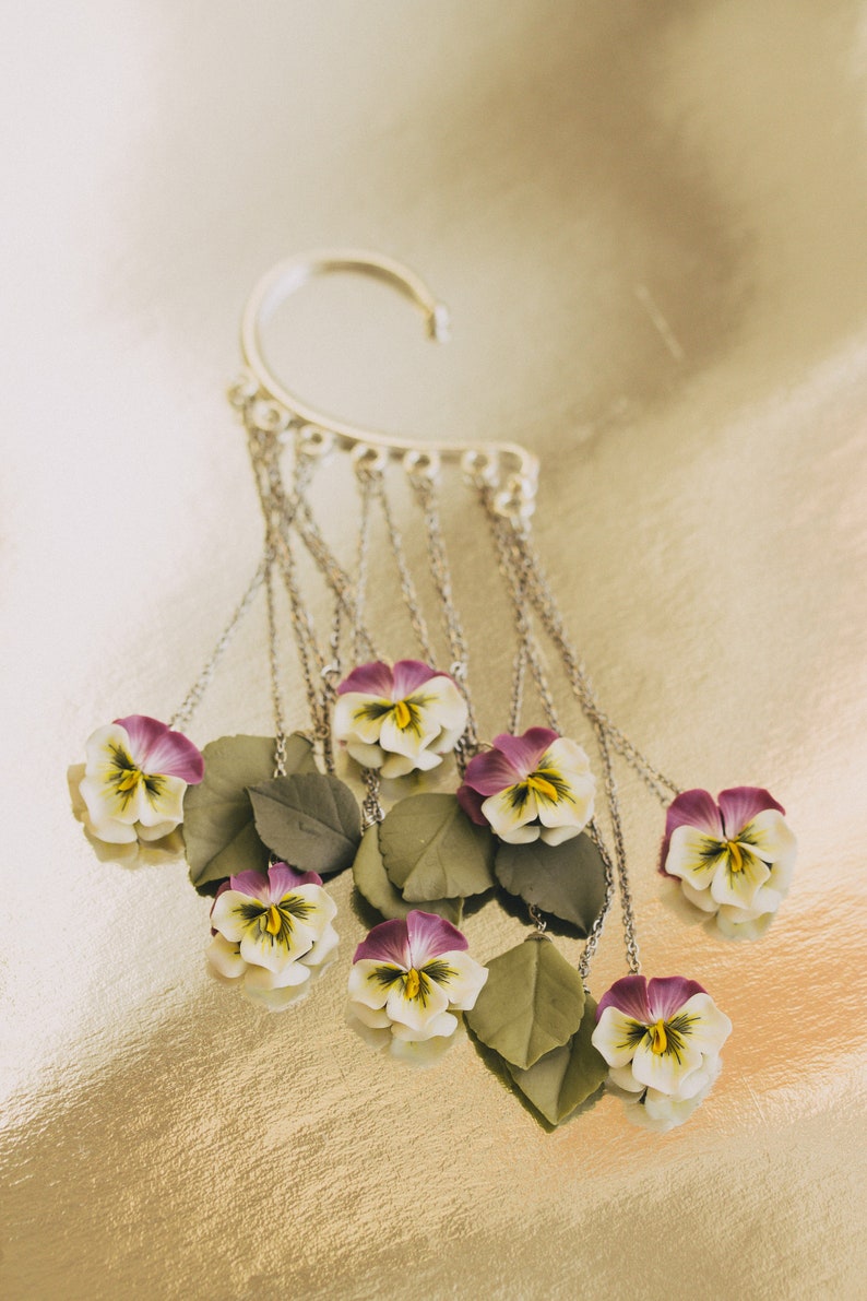 May include: A silver ear cuff with multiple chains hanging down, each chain ending with a small purple and white flower with green leaves.