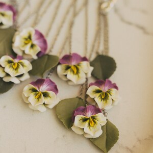 May include: A silver chain necklace with multiple pendants featuring purple and white pansies with green leaves.