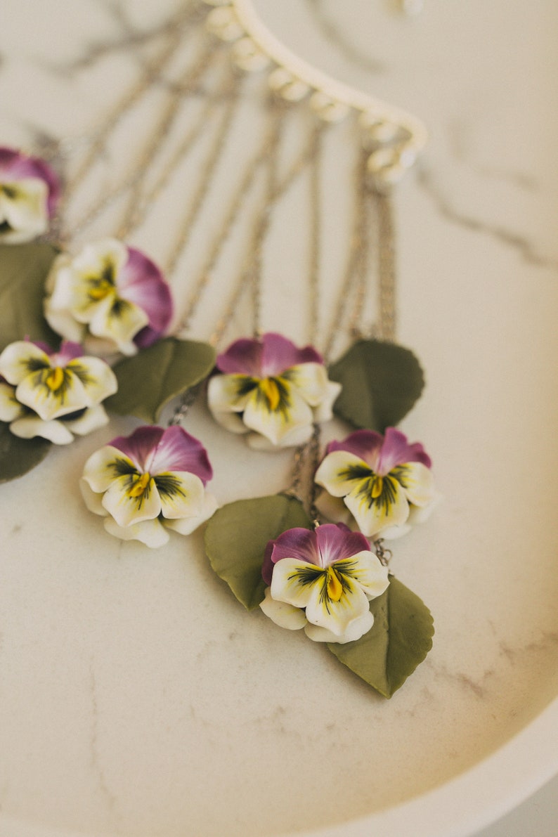 May include: A silver chain necklace with multiple pendants featuring purple and white pansies with green leaves.
