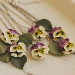 May include: A silver chain necklace with multiple pendants featuring purple and white pansies with green leaves.