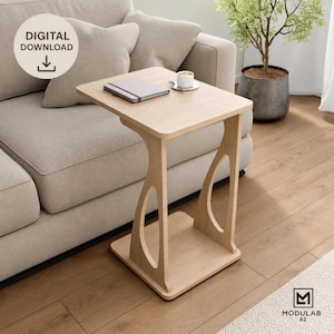 Puede incluir: Una mesa auxiliar de madera clara en forma de C con una superficie rectangular y una base con dos aberturas. Sobre la mesa hay un cuaderno gris cerrado y una taza blanca sobre un platillo. Se observa el texto DIGITAL DOWNLOAD en la imagen.