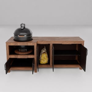 May include: A dark wood outdoor kitchen island featuring a built-in black ceramic grill on the left side. The unit includes three storage compartments with open doors, revealing black interior shelving and a yellow bag stored inside the center section.