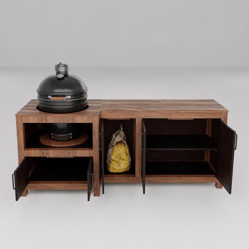 May include: A dark wood outdoor kitchen island featuring a built-in black ceramic grill on the left side. The unit includes three storage compartments with open doors, revealing black interior shelving and a yellow bag stored inside the center section.