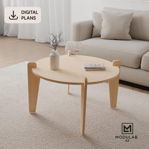 Pode incluir: Uma mesa de centro redonda de madeira clara com três pernas entrelaçadas. A superfície da mesa contém um vaso branco com ramos finos, um copo de vinho e um livro. Uma etiqueta indica DIGITAL PLANS e um logótipo mostra MODULAB 42.