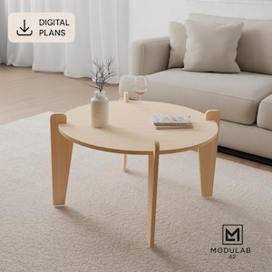 Puede incluir: Una mesa de centro de madera clara con una superficie circular y tres patas verticales que sobresalen por encima del tablero. Sobre la mesa hay un jarrón blanco con ramas finas, una copa de vino y un libro. El texto DIGITAL PLANS es visible.