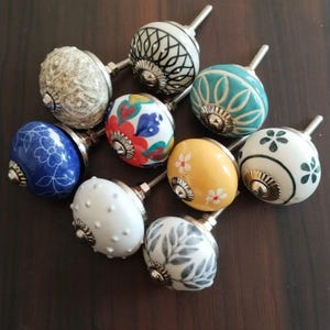 Peut inclure: Un assortiment de boutons de meubles décoratifs avec divers motifs et couleurs. Les boutons présentent des motifs floraux, géométriques et à pois. Les couleurs incluent le bleu, le blanc, le jaune et le turquoise. Chaque bouton a une tige métallique.