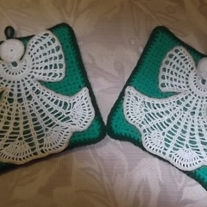 May include: Two crocheted angel pot holders with white lace designs on a green background.