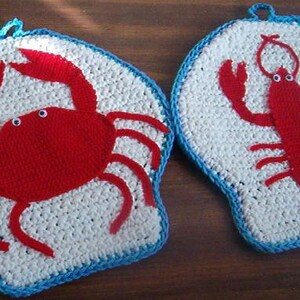 以下が含まれることがあります： カニとロブスターの形をした、2つの編まれた鍋つかみ。どちらも赤色で、白と青のアクセントが付けられています。