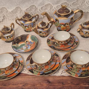 May include: A porcelain tea set featuring a teapot, sugar bowl, creamer, and three teacups with matching saucers and plates. Each piece is decorated with colourful illustrations of figures in traditional attire, gold trim, and black, orange, and blue accents.