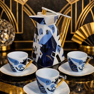 Könnte beinhalten: Ein weiß-blaues Porzellan-Teeservice mit goldenen Akzenten. Das Set besteht aus einer hohen Teekanne und drei Tassen mit Untertassen. Das Design zeigt geometrische Formen und Muster in Blau und Schwarz.
