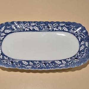 Puede incluir: Una taza de cerámica blanca con un asa negra y el texto "But First, Coffee" en un estilo manuscrito. La taza está sobre una superficie blanca.