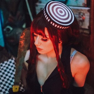 Puede incluir: Una mujer con el pelo largo y rojo lleva una blusa negra y medias de rejilla. Lleva un sombrero a rayas blancas y rojas con una banda negra.