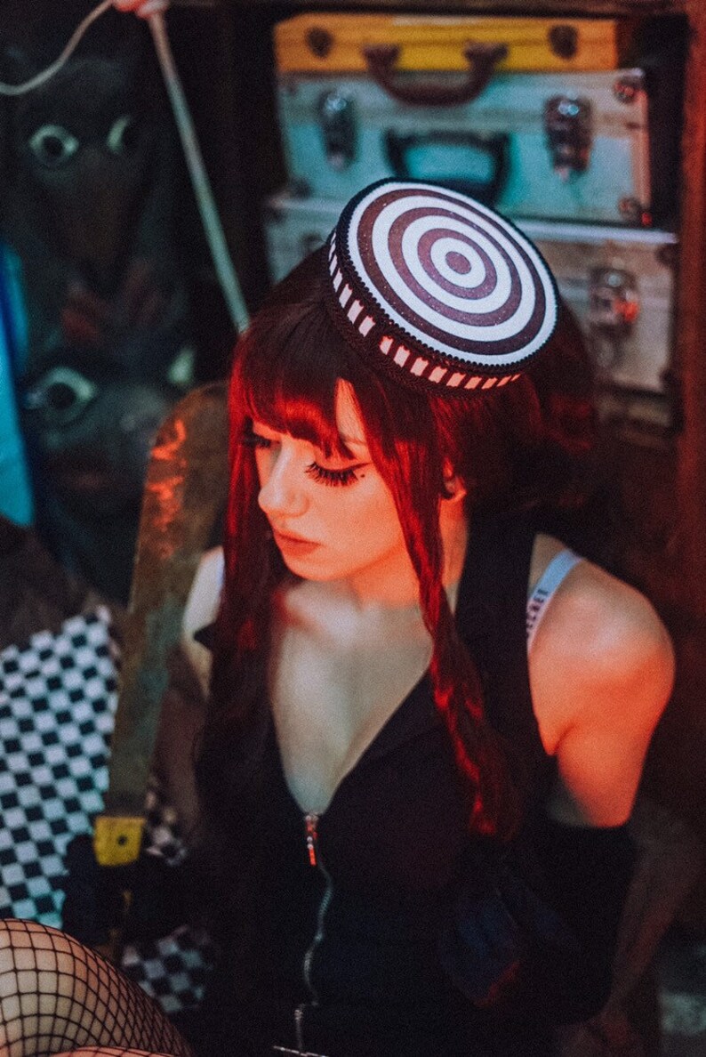 Puede incluir: Una mujer con el pelo largo y rojo lleva una blusa negra y medias de rejilla. Lleva un sombrero a rayas blancas y rojas con una banda negra.