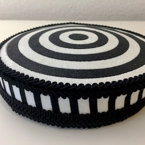 Puede incluir: Soporte para pastel redondo en blanco y negro con una cinta rayada en blanco y negro y un ribete trenzado negro. La parte superior del soporte tiene un dise&ntilde;o de c&iacute;rculos conc&eacute;ntricos en blanco y negro.
