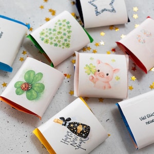 Op de afbeelding: Een verzameling kleine, verpakte cadeautjes met verschillende ontwerpen. Sommige cadeautjes tonen een hart van klavers, een ster, een varken met een klavertjevier en een champagnefles met de tekst "Happy New Year".