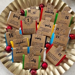 Könnte beinhalten: Ein goldfarbenes, gerüschtes Tablett hält einen Weihnachtskalender. Der Kalender zeigt kleine, nummerierte Päckchen mit festlichen Illustrationen und Text. Rote Ornamente und Tannenzweige ergänzen das Thema.