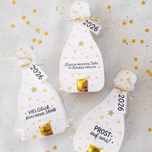 Puede incluir: Tres etiquetas de regalo con forma de botella de champ&aacute;n con patrones de estrellas doradas y el a&ntilde;o "2026" en las etiquetas. Cada etiqueta tiene una frase alemana diferente, como "&iexcl;Feliz A&ntilde;o Nuevo!"