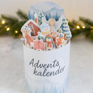 Könnte beinhalten: Ein weißer Adventskalender mit einer Winterlandschaft und der Aufschrift "Advents kalender". Der Kalender zeigt Pop-up-Figuren eines Rentiers, eines Schneemanns, eines Engels und anderer festlicher Charaktere. Zahlen sind sichtbar.