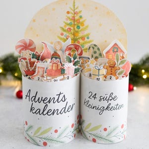 Könnte beinhalten: Festlicher Adventskalender mit zwei weißen zylindrischen Behältern, die mit weihnachtlichen Illustrationen verziert sind. Die Behälter sind mit einer Girlande aus grünen Blättern und roten Beeren geschmückt. Der Text "Adventskalender" und "24 süße Kleinigkeiten" ist aufgedruckt.