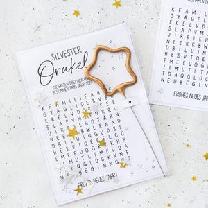 Könnte beinhalten: Eine weiße Karte mit dem Text Silvester Orakel und einem Suchsel-Gitter auf Deutsch, ergänzt durch einen goldenen sternförmigen Stab. Die Karte ist mit kleinen goldenen und silbernen Sternkonfetti sowie dem Text Frohes Neues Jahr versehen.
