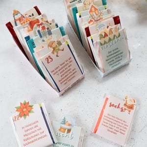 Könnte beinhalten: Adventskalender mit nummerierten Tagen, mit festlichen Illustrationen und Text. Der Kalender enthält kleine Päckchen mit verschiedenen Designs, perfekt zum Countdown bis Weihnachten. Das Bild enthält Text auf Deutsch und anderen Sprachen.