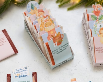May include: A collection of small rectangular packets arranged in a box, each featuring colorful holiday illustrations and German text. The packets display festive graphics like a snowman, gingerbread, and candy canes, with printed numbers and humorous holiday sayings.